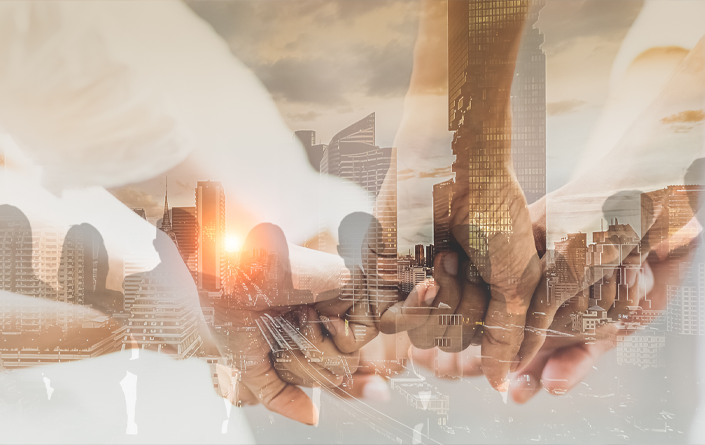 Double exposure photo of hands joined together over silhouetted city background with business buildings.